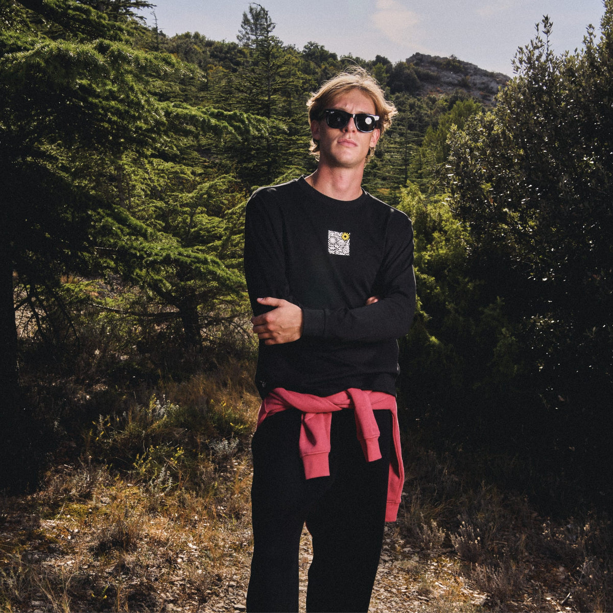 Homme en sweat noir Sun Valley, veste rouge nouée à la taille, dans la forêt